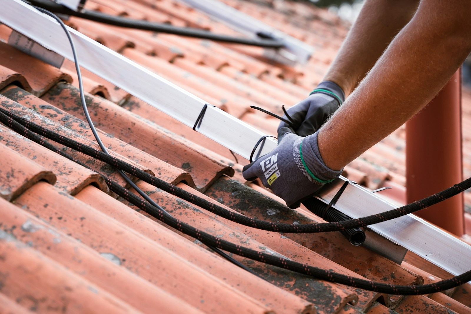Handen met werkhandschoenen bevestigen een kabel op een dak met rode pannen